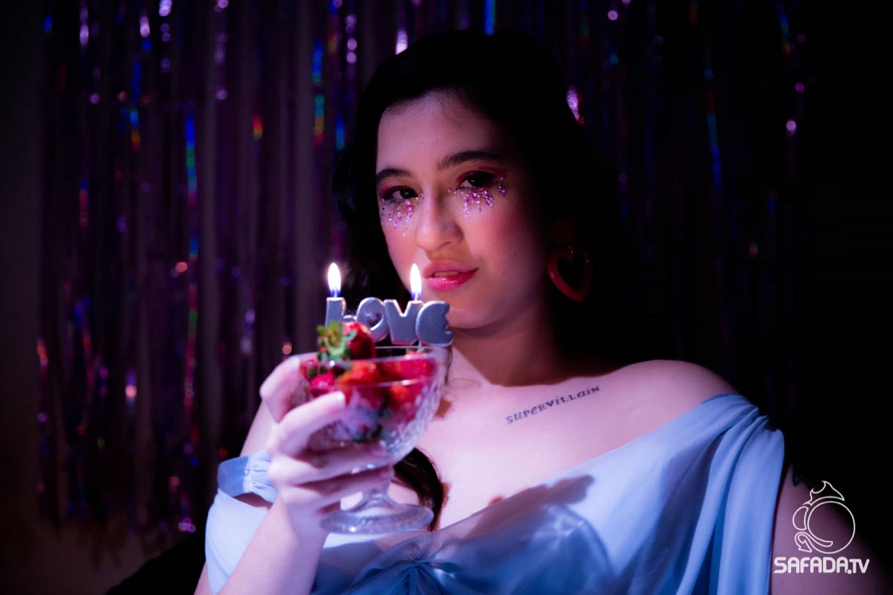 Nittie como a canceriana de Safadezas Astrológicas, de azul, segurando uma taça