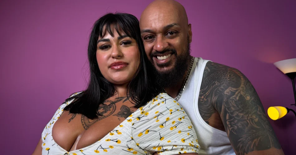 Casal sorridente abraçado diante de uma parede roxa