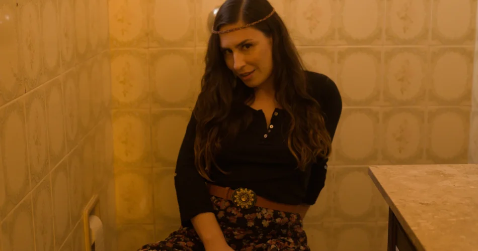 Emme White sentada num banheiro de azulejos, em visual boho